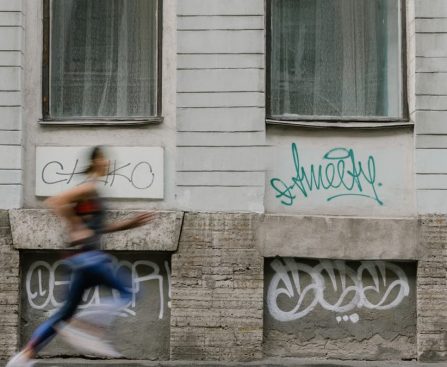 Blurred motion of a woman running past a graffiti-covered urban wall. Captures dynamic energy.